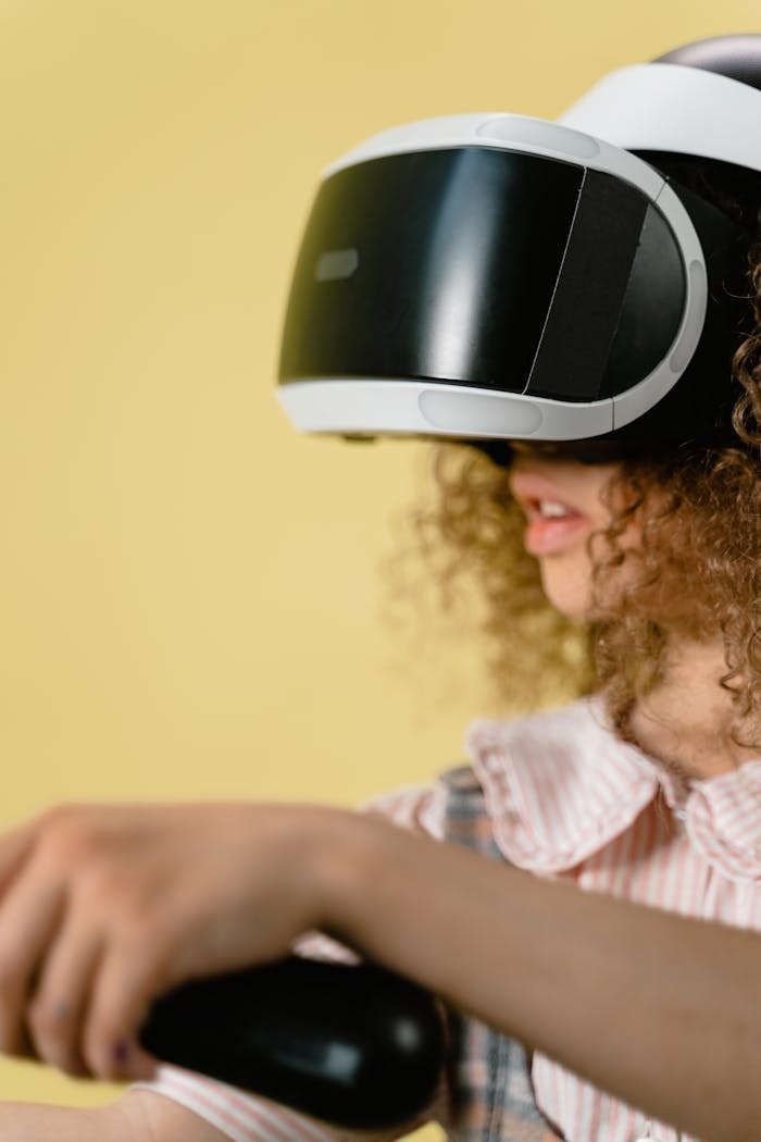 Curly-haired child using VR goggles indoors with a yellow background.