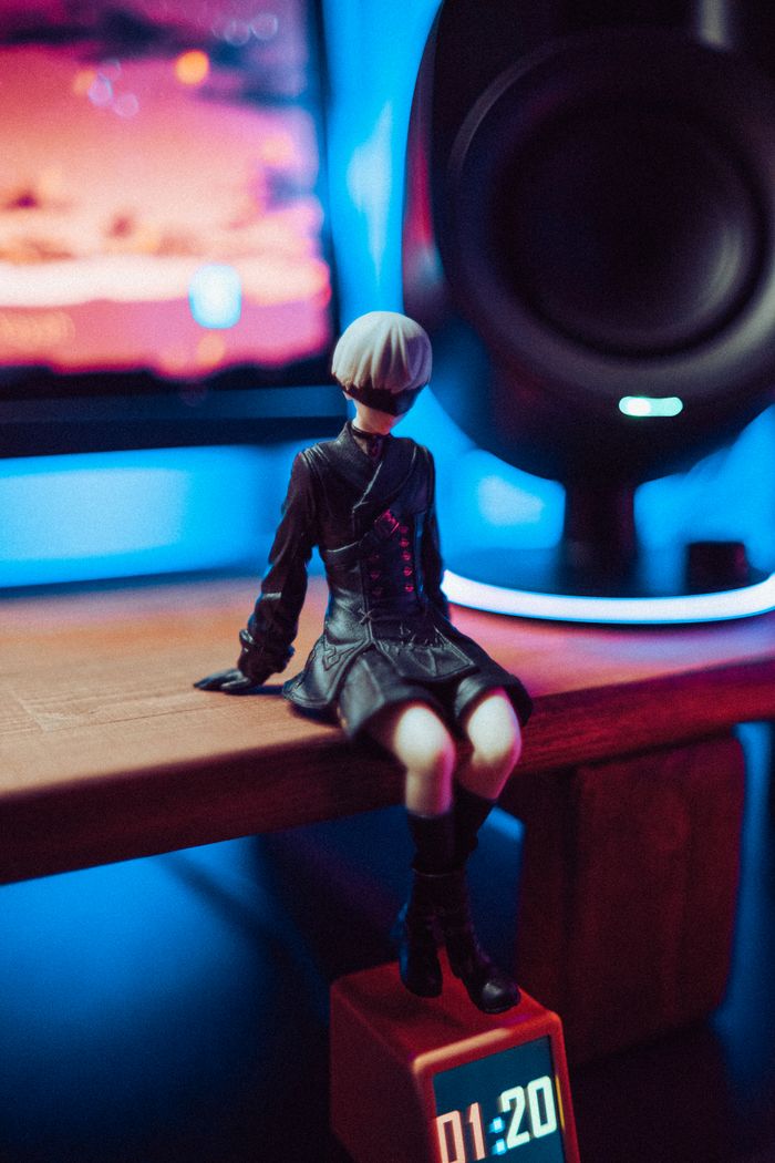 services-01 A stylish figurine sits on a desk lit by colorful neon lights with a digital clock display.